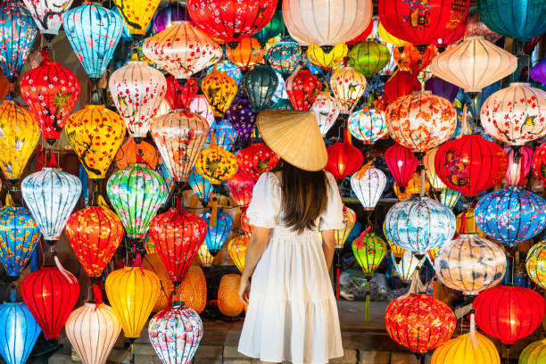 Rear view of Asian traveler woman is enjoy watching lanterns in old town Hoi An, Woman choosing a lamp at Hoi An ancient town, Vietnam